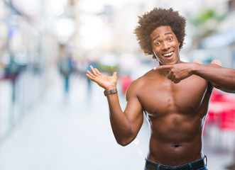 Fototapeta na wymiar Afro american shirtless man showing nude body over isolated background amazed and smiling to the camera while presenting with hand and pointing with finger.
