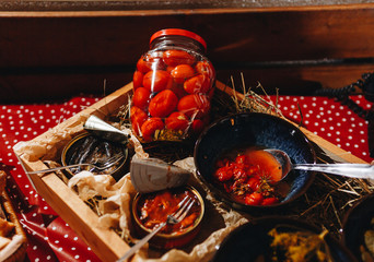 Homemade glass jars of pickled fresh cucumbers, juicy tomatoes, sweet zucchini in a wicker box on a wooden background. Stock of food. Autumn concept. Top view.