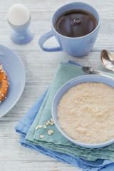 Oatmeal porridge bowl on the white wooden background.
