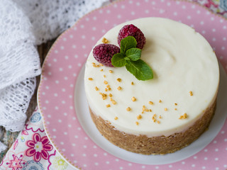Cheesecake with raspberries and mint on a pink plate on a wooden table with floral fabric and laces. Close up, copy space, selective focus