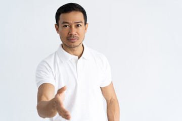 Serious confident guy offering handshake. Handsome young man dressed in white polo ready to shake partner hand. Deal concept