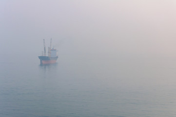 View of the cargo ship floating on the sea through the thick fog