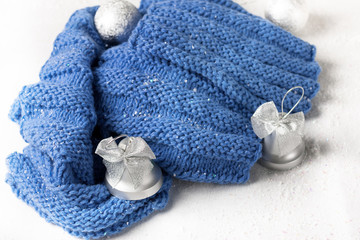 Fototapeta na wymiar wool knitted scarf handmade deep blue colow with silver christmas toys on the snow table white