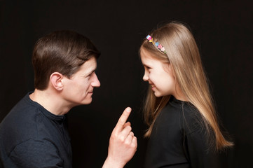 The father teaches his daughter on a black background, the girl carefully listens to her father