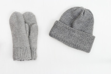 Knitted grey mittens and hat on white background. View from above. Copy space.