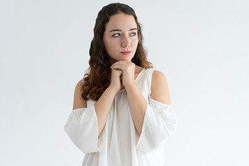 Portrait of concentrated young woman standing with clasped hands and looking away. Pretty Caucasian woman thinking about something. Concentration concept