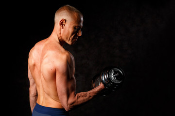 Obraz na płótnie Canvas Muscular bodybuilder guy doing exercises with dumbbell over black background