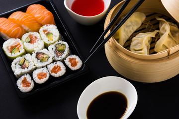 Dumplings or gyoza served in traditional steamer and sushi on black background.