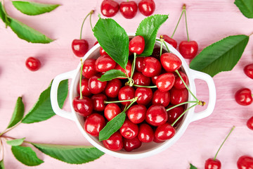 Red cherry in white bowl on pink background.