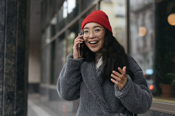 Excited happy Korean woman talking by mobile phone and laughing, she heard good news. Portrait of...
