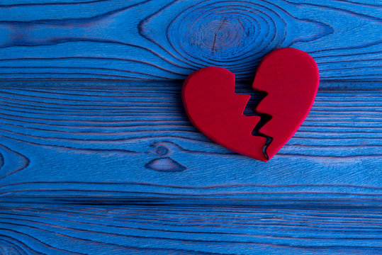 red heart divided in half on a blue wooden background. parting, divorce, quarrel.