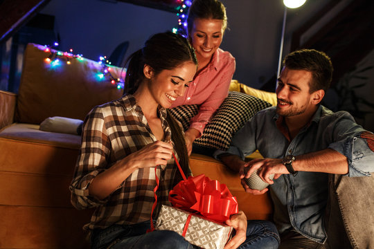Young woman sitting with her friends on Christmas evening.Celebration concept.Unpacking gift.