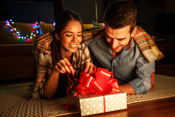 Young woman opens a gift which she got from her husband.Christmas evening  concept.