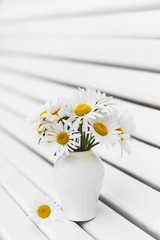 Chamomiles in the vase on a white wooden background. Flowers