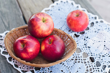 Autumn harvest. Red ripe apples in a wicker basket on a knitted napkin on a table in the garden on a Sunny day. Rustic style