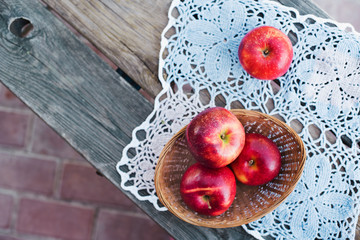 Autumn harvest. Red ripe apples in a wicker basket on a knitted napkin on a table in the garden on a Sunny day. Rustic style