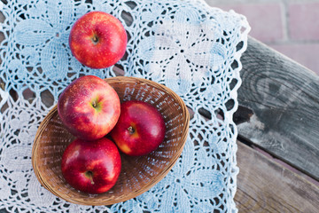 Autumn harvest. Red ripe apples in a wicker basket on a knitted napkin on a table in the garden on a Sunny day. Rustic style	