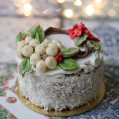 White New Year or Christmas cake decorated with cream poinsettia flowers, pine cones, cottons and spruce twigs on a colorful table. A birthday cake for those born in winter.Copy space, selective focus