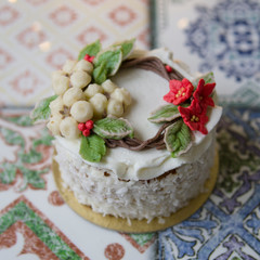 White New Year or Christmas cake decorated with cream poinsettia flowers, pine cones, cottons and spruce twigs on a colorful table. A birthday cake for those born in winter.Copy space, selective focus