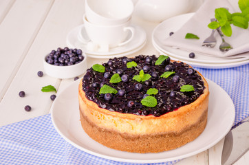 Delicious cream cheesecake with lemon zest and blueberry jam on a plate on a white wooden background