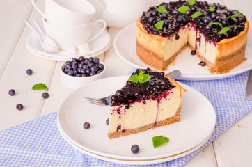 Delicious cream cheesecake with lemon zest and blueberry jam on a plate on a white wooden background