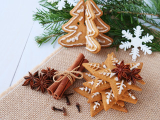 Christmas background with gingerbread figurines, cinnamon, star anise, cloves and fir branches over burlap on the table.