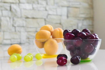 Bowl of apricots and a bowl of cherries on a bright table in the Studio. Healthy food.