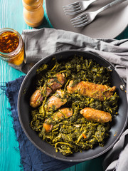 Italian sausages with rapini broccoli in a skillet with table setting on green wooden table