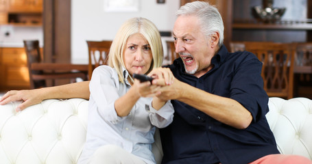 Mature couple fighting for remote control on a sofa