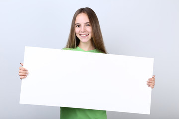 Fototapeta premium Young girl holding blank board on grey background