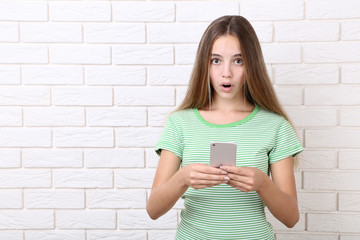 Surprised girl with smartphone on brick wall background