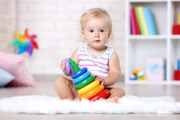 Baby girl sitting on white carpet with toy