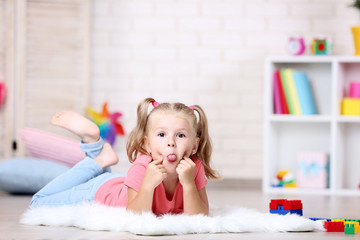 Little girl lying on white carpet and showing tongue