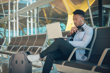 Young businessman is seated in the airport working with a laptop and carrying a suitcase waiting...
