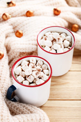Cappuccino with marshmallows in mugs and knitted scarf on wooden table