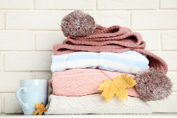 Folded sweaters with cup, scarf and maple leafs on brick wall background