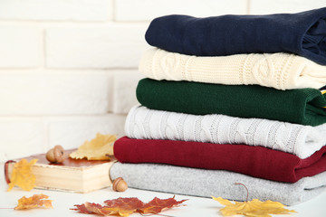 Stack of folded sweaters with acorns and autumn leafs on brick wall background