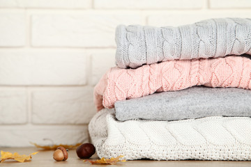 Stack of folded sweaters with acorn, chestnut and autumn leafs on brick wall background