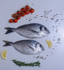 Two fresh dorada fishes with cherry tomatoes, rosemary, lemon and pepper on light wooden background