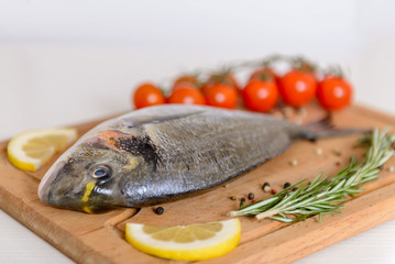 Fresh dorado fish with cherry tomatoes, rosemary, lemon and pepper on wooden cutting board