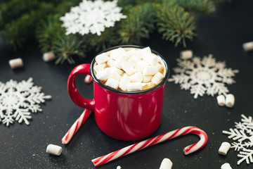 Christmas background. Happy new year. Red mug with hot chocolate, white marshmallows and candy in the shape of a Christmas tree on a black background. Selective focus.