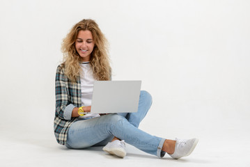 Beautiful blonde woman sitting on floor with laptop on white background