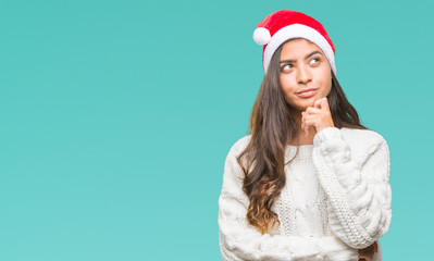 Young arab woman wearing christmas hat over isolated background with hand on chin thinking about question, pensive expression. Smiling with thoughtful face. Doubt concept.