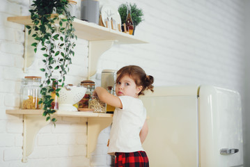 Cute little girl in red pajamas, preparing cookies in the kitchen at home. Sits on the kitchen table and helps mom prepare a festive Christmas dinner