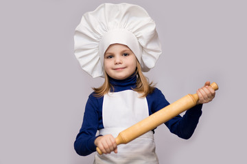 Children cook. Happy little girl in chef uniform holds rolling pin isolated on white background.