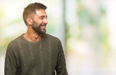Adult hispanic man wearing winter sweater over isolated background looking away to side with smile on face, natural expression. Laughing confident.