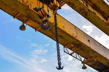 Hook gantry crane on the chain for lifting heavy loads on the background of a metal beam and a blue...