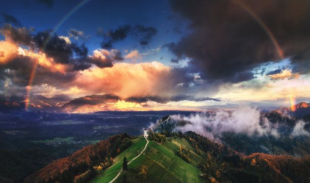 Jamnik, Slovenia - Aerial view of rainbow over the church of St. Primoz in Slovenia near Jamnik with beautiful clouds and Julian Alps at background.