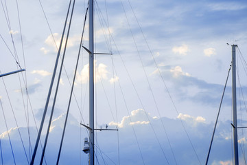 Masts of sailing yachts against the blue sky with clouds