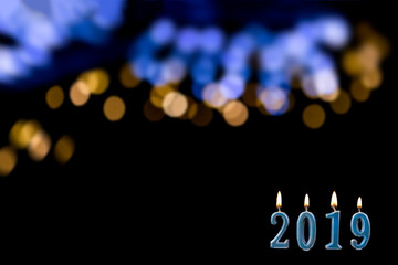 blue text of 2019 lit candle with flame over shinny blurry blue gold, on black wall. New year concept. background,